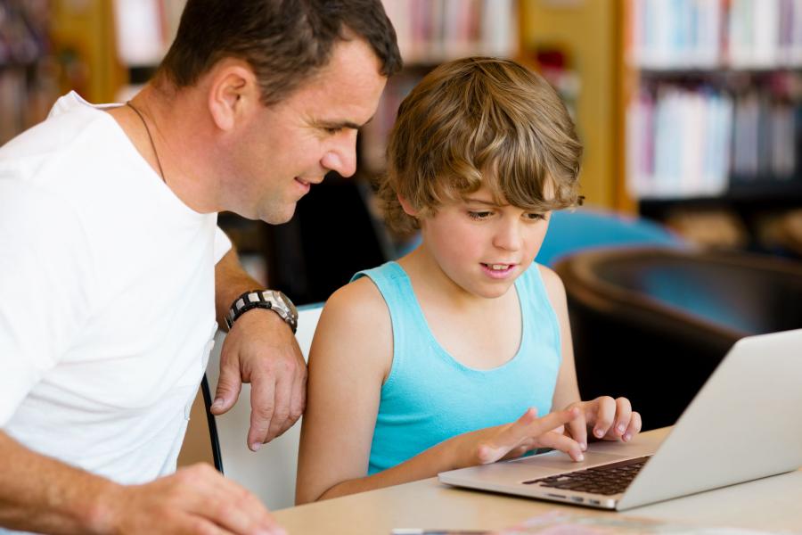 Boy on his computer with father sitting next to him and looking on