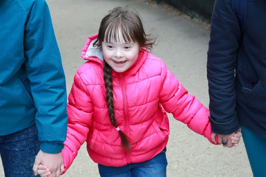 Young girl with a disability holding her parents' arms on a walk