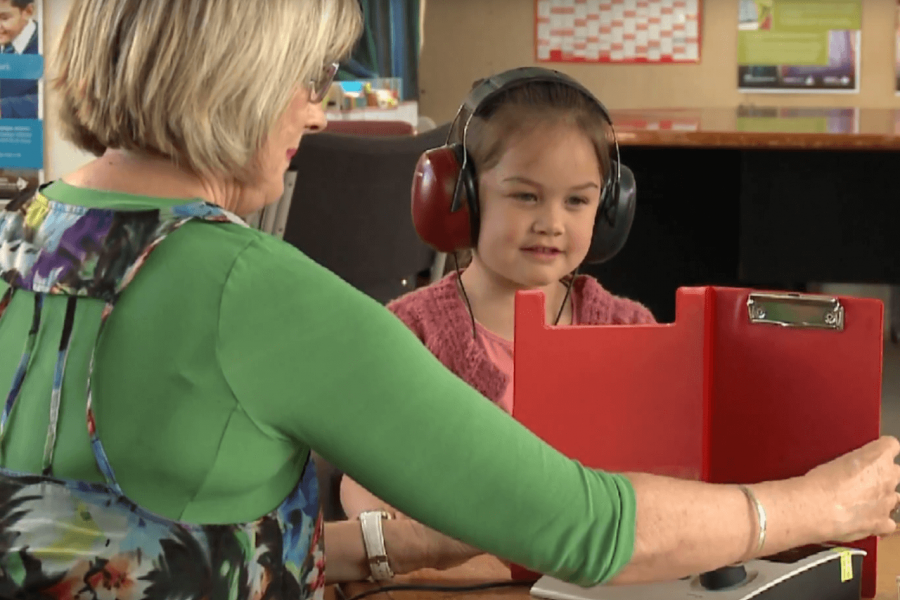 A vision hearing technician testing a young girl with headphones on