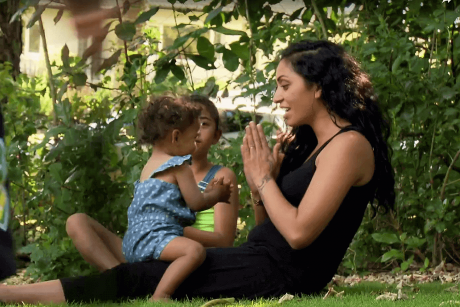 Mother sitting on the grass outside with ter toddler on her knee and her older son sitting alongside