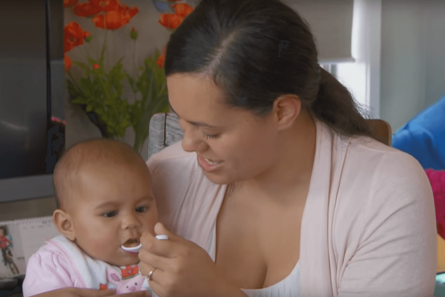 Mother with her baby on her lap, giving her baby a spoon of pureed baby food