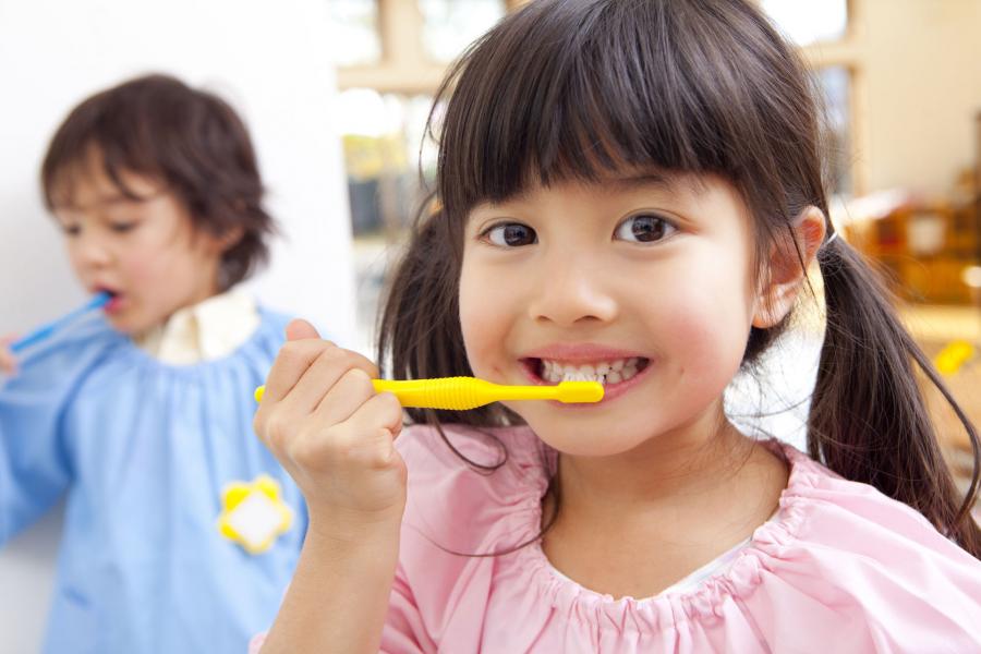 Young girl brushing her teeth with another child brushing teeth in the backgroud