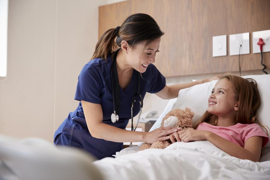 Doctor standing next to a girl in a hospital bed with her teddy 