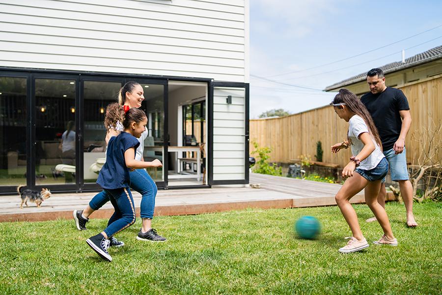 A family of 2 adults and 2 kids playing with a ball on the lawn by their house