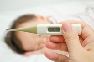 A hand holding a thermometer in front of a little child in bed