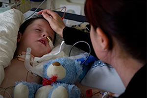 A boy sick in hospital with tetanus with parent sitting by bed