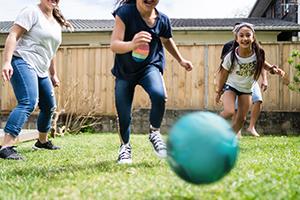 A family - 2 adults and 2 kids running for a ball on grass