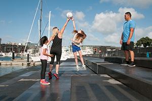 A family of 2 adults and 2 kids playing a ball game by the water 