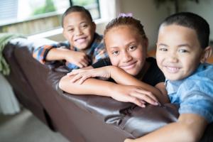 Three tamariki smiling while sitting on the couch