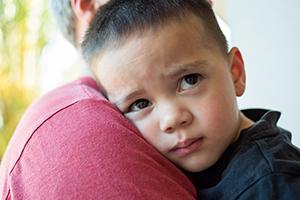 A young upset boy being hugged by his father